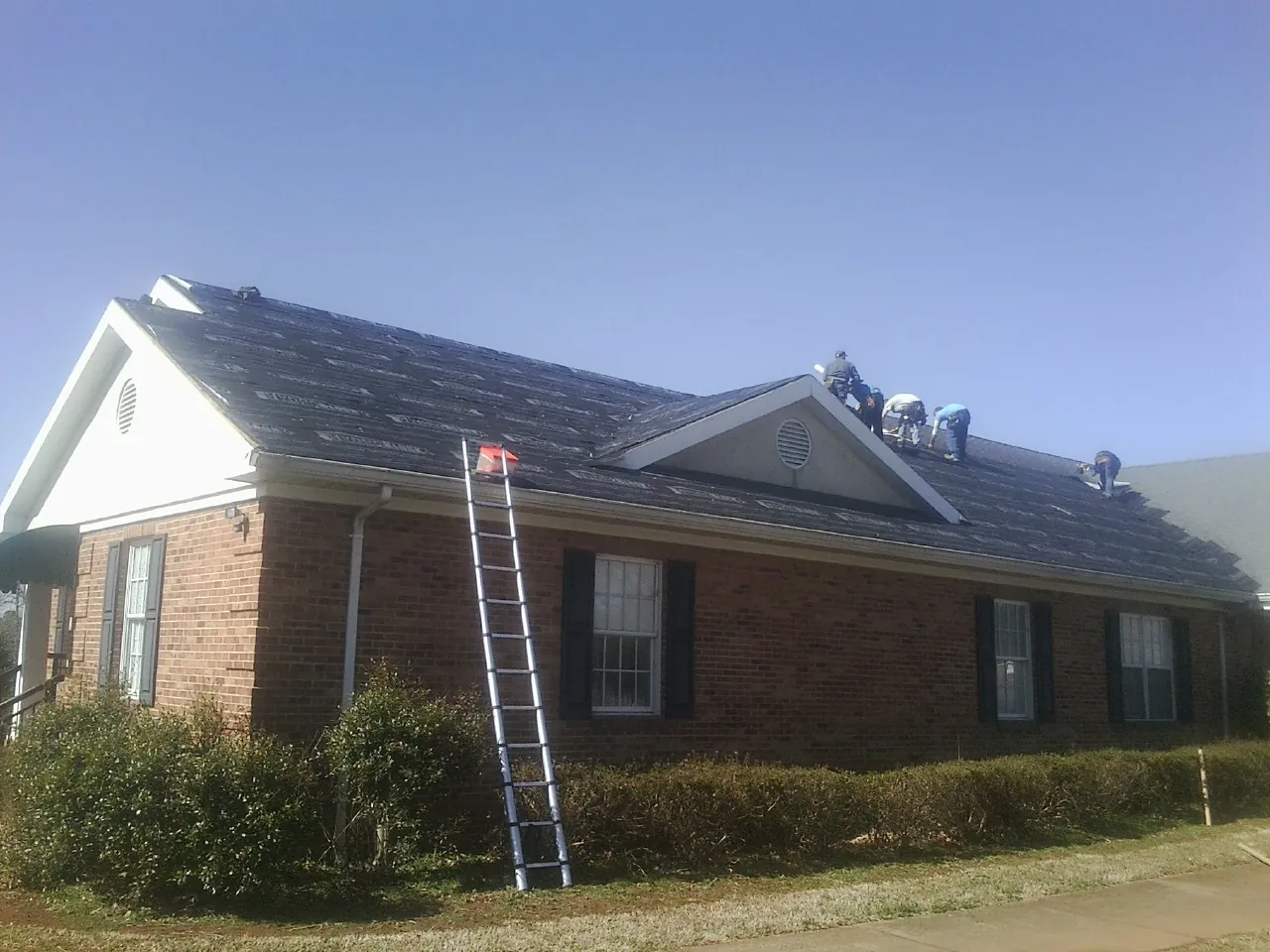 Crew tearing shingles off a brick ranch roof with a ladder set — Emergency Roof Repair work by our crew in Tarrs