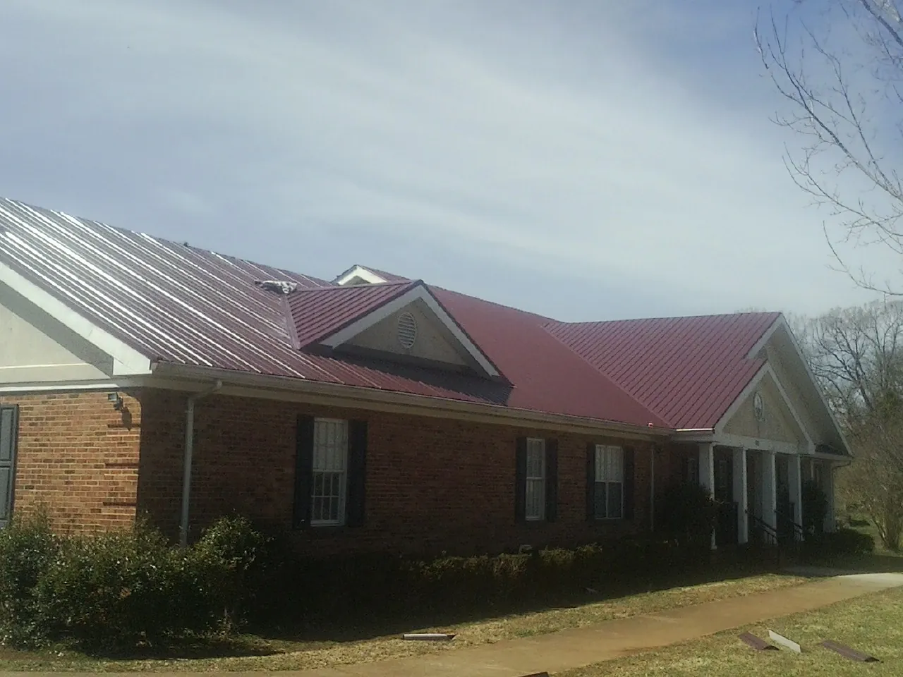 Red metal roof with gabled entries on a long brick building, from a Hail Damage Roof Repair job in Tarrs