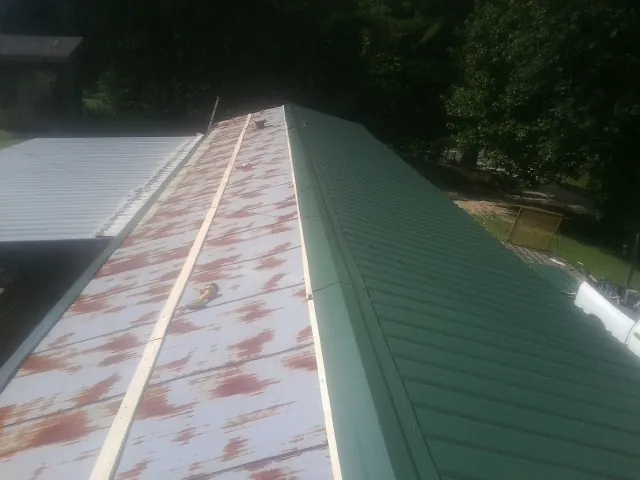 Old rusted panels beside newly installed green metal roofing — Wind Damage Roof Repair by Roofing Brothers in Tarrs