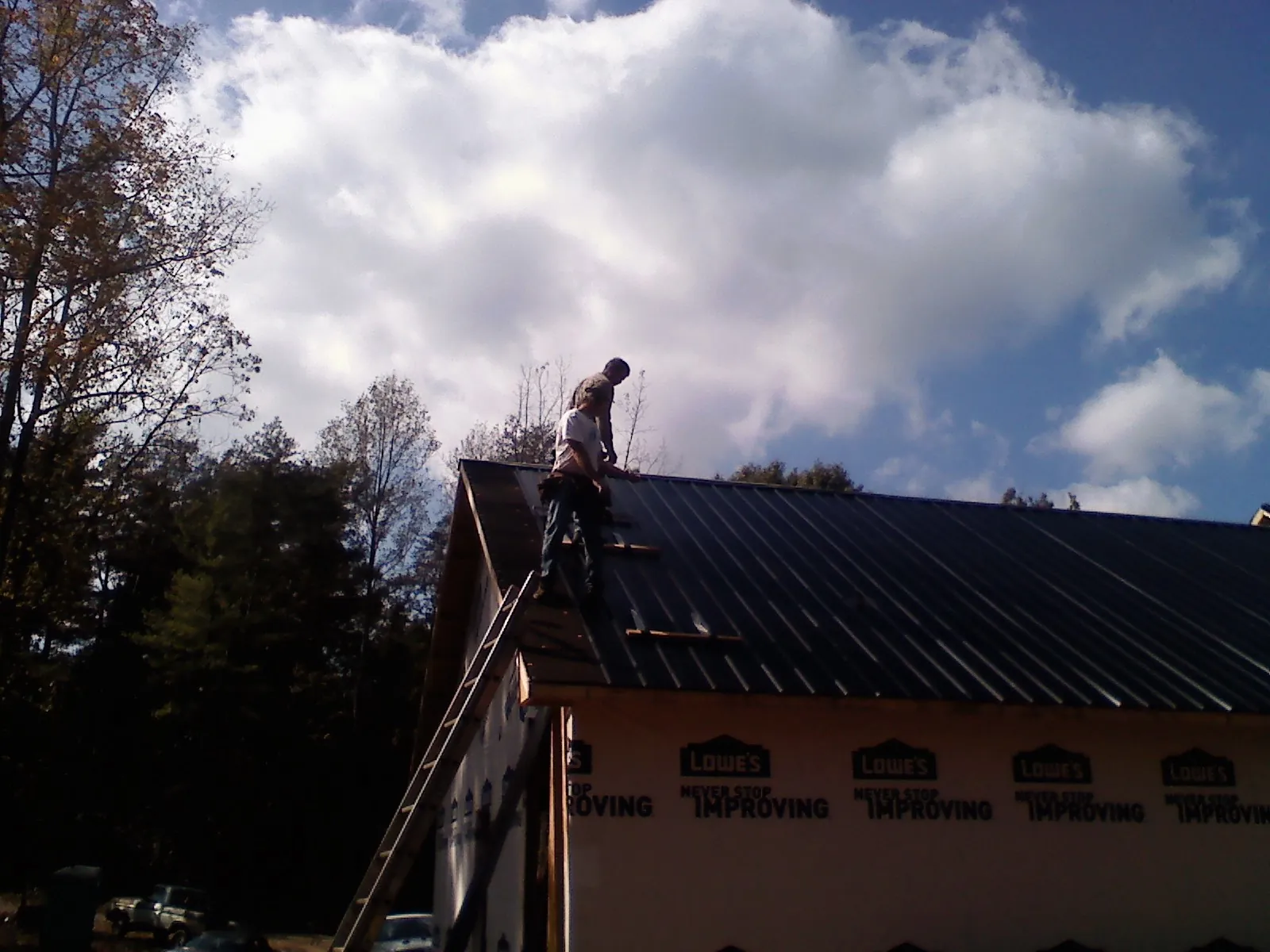 Roofer fastening dark metal panels high against a cloudy sky, from a Roof Inspection job in Tarrs