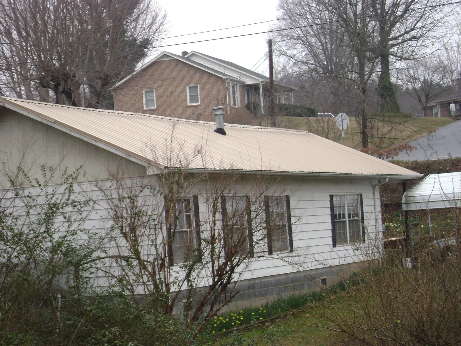 Tan metal roof on a white sided house set into a hillside — Commercial Roofing by Roofing Brothers in Tarrs