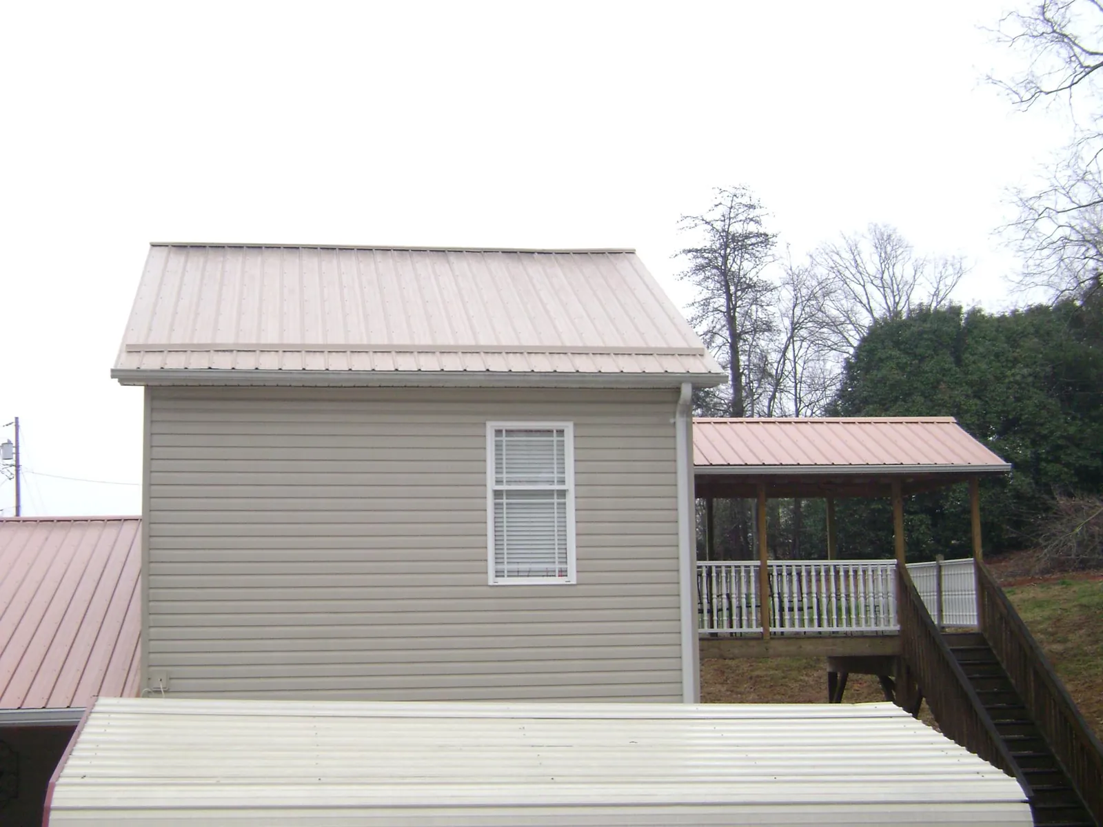 Tan metal roofs on a two story addition and attached porch, from a Roof Replacement job in Tarrs