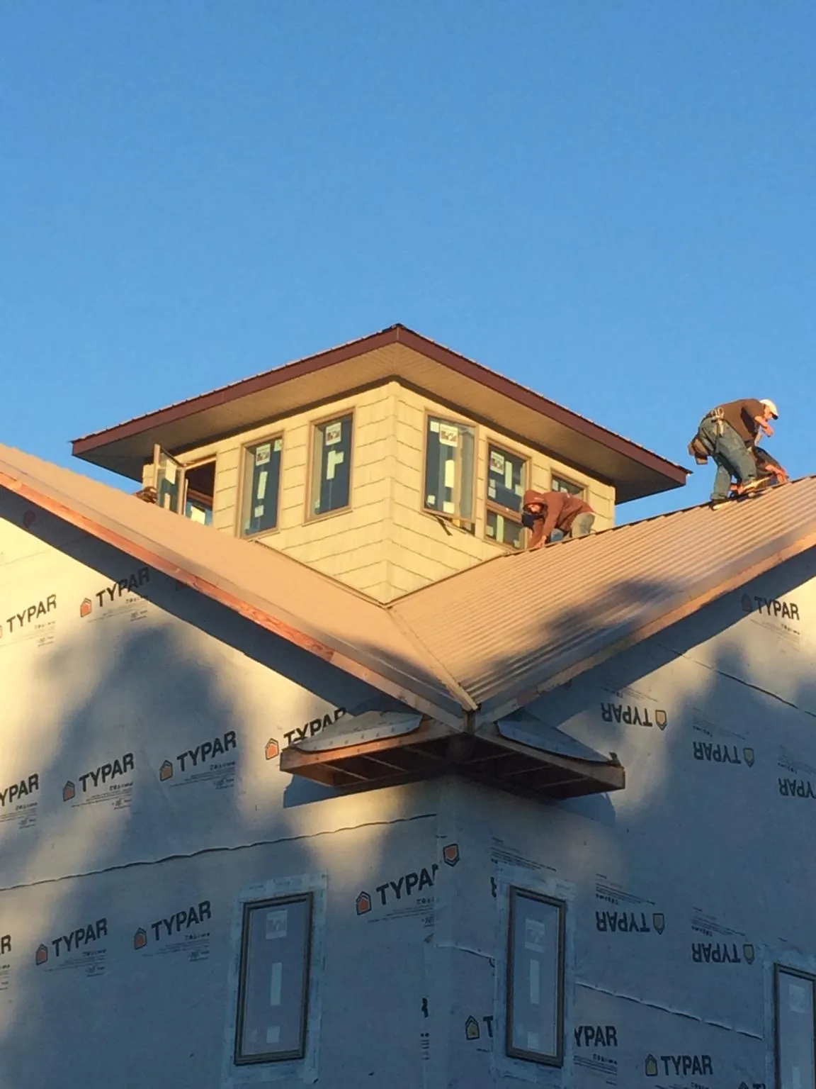 Roofers working around a rooftop cupola on a new metal roof at sunset — Roof Waterproofing in Tarrs by Roofing Brothers